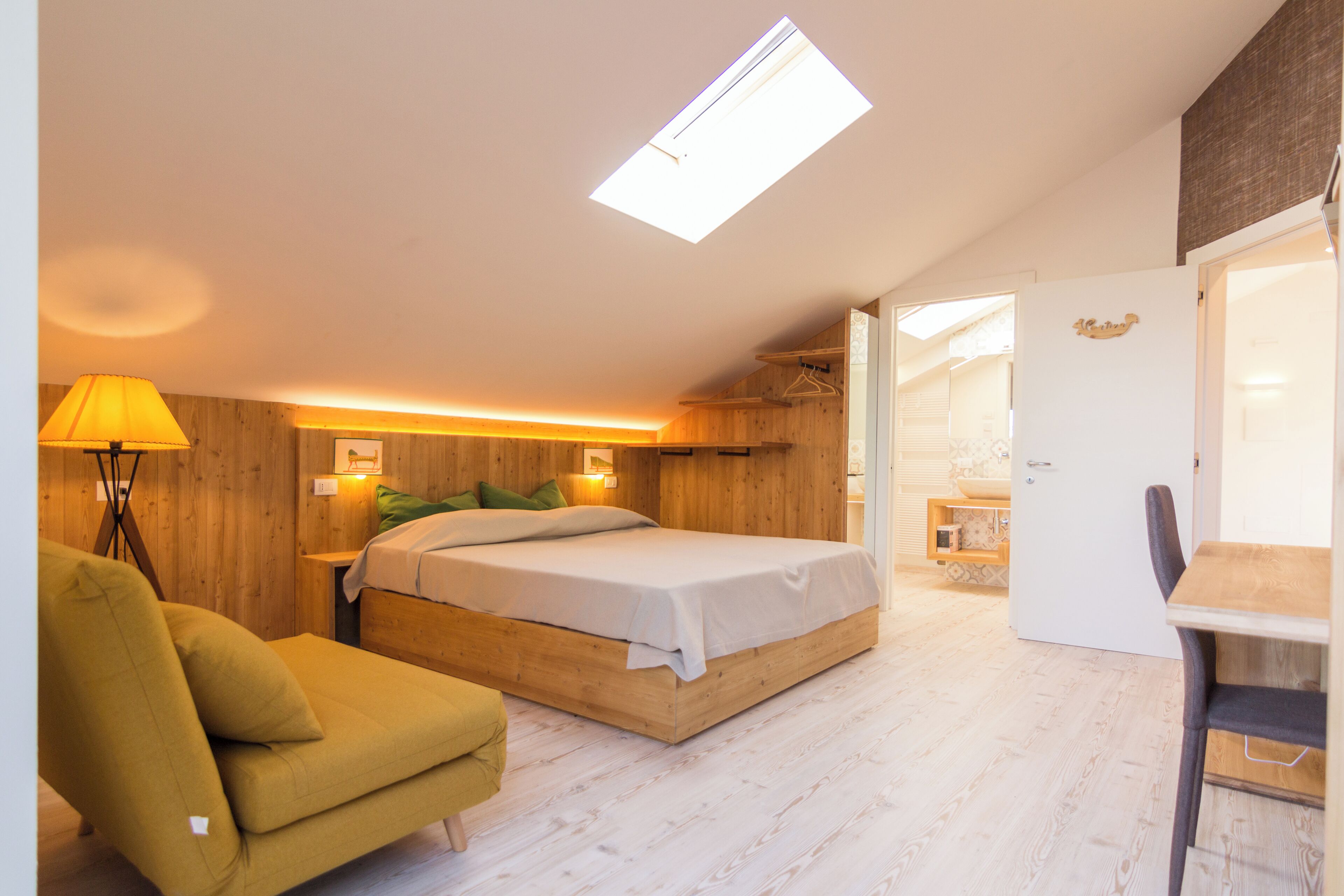Un dormitorio con cama, una silla, un escritorio y un tragaluz.
