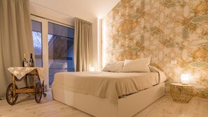 Un dormitorio con una cama grande, una mesita con botellas, una silla de ruedas y un papel tapiz estampado.
