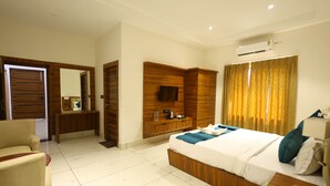 Une chambre d’hôtel comprenant un lit, une armoire en bois, une télévision, un bureau et une salle de bain avec un miroir.