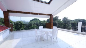 Un balcon avec une table et des chaises, une vue sur la verdure et un sol carrelé.
