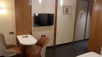 A modern hotel room with a bed, a small table, two chairs, a TV, and a wardrobe.