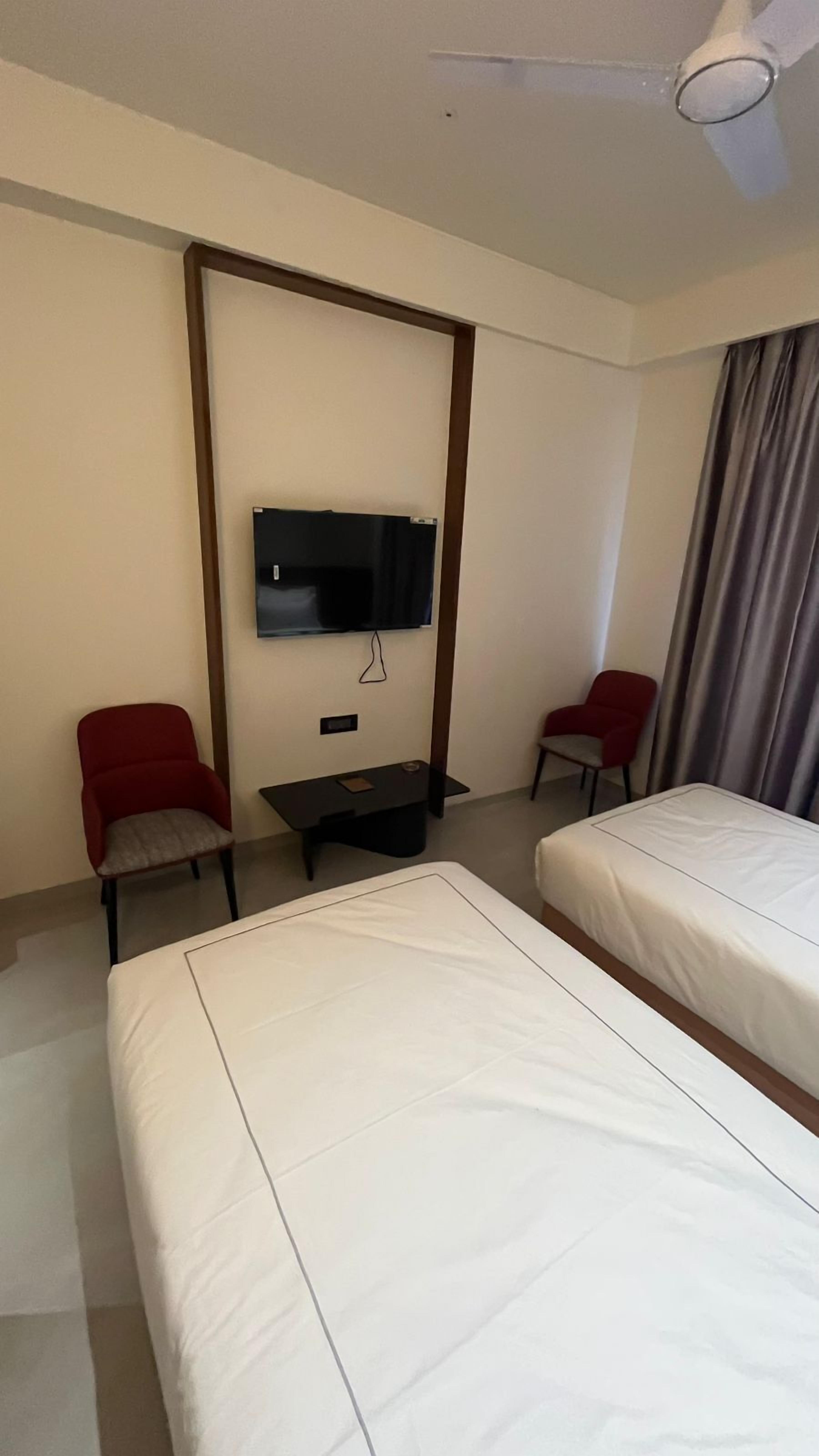 Een hotelkamer met twee bedden, een aan de muur bevestigde televisie, een klein tafeltje en twee stoelen.