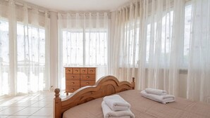 Een slaapkamer met een houten bed, een dressoir en dunne gordijnen.