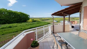 Een balkon met een tafel en stoelen, een bloempot en uitzicht op een groen landschap.