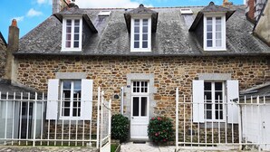 A stone house with a white door, two windows with shutters, and a small garden with a red flower bush. - Bernard & Bernadette, la familiale près de l'étang (Châtelaudren-Plouagat)