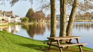 A picnic table by a calm lake with trees and houses in the background. - Bernard & Bernadette, la familiale près de l'étang (Châtelaudren-Plouagat)