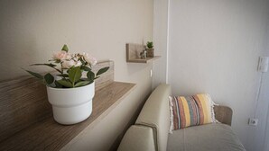Una sala de estar con un sofá, una planta en maceta y un estante pequeño con adornos.
