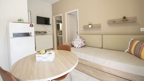 Un espacio habitable compacto con kitchenette, un sofá, una mesa de comedor y un televisor montado en la pared.