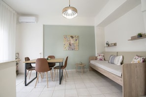 A modern living space with a dining area, a sofa, a small round table, and a hanging light fixture. - Forest View Apartment 1 by RentalsPro (Fourka)
