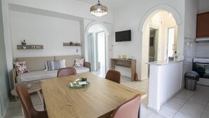 A dining area with a wooden table and chairs, a sofa with cushions, a TV mounted on the wall, and an archway leading to another room. - Forest View Apartment 1 by RentalsPro (Fourka)