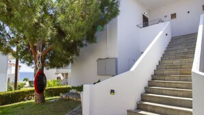 Un bâtiment blanc avec un escalier menant à un balcon, entouré de verdure et offrant une vue sur la mer.