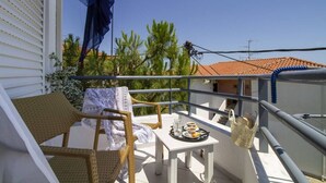 En balkon med fletstole, et lille bord med en bakke mad og udsigt til en bygning med et tagdækket tag og palmer.