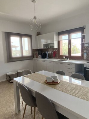 Una cocina moderna con armarios blancos, una mesa de comedor con sillas y una lámpara colgante.