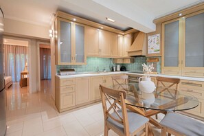 A modern kitchen with wooden cabinets, a glass dining table, and a view of the living area. - Ivory Cozy Home by RentalsPro - Nea Moudania (Nea Moudania)