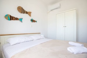 Un dormitorio con cama, almohadas blancas, edredón blanco, una puerta blanca y un equipo de aire acondicionado.