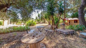 An outdoor seating area with wooden tables and chairs, surrounded by trees and a small wooden structure.