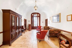 Um corredor espaçoso com um armário de madeira imponente, poltronas estofadas em vermelho e um candelabro.