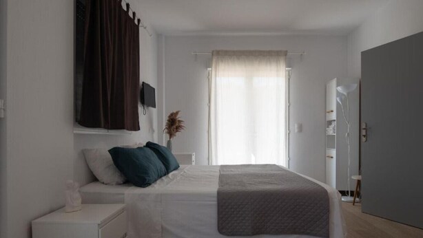 Un dormitorio con cama, mesitas de noche, un armario y una ventana con cortinas.