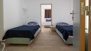 Una habitación con dos camas, una mesita y una puerta.