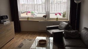 Een woonkamer met een bank, een salontafel, een tv op een kast, en een raam met gordijnen.