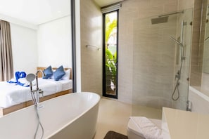 Een moderne badkamer met een vrijstaand bad, een douchegedeelte en een bed met blauwe kussens.