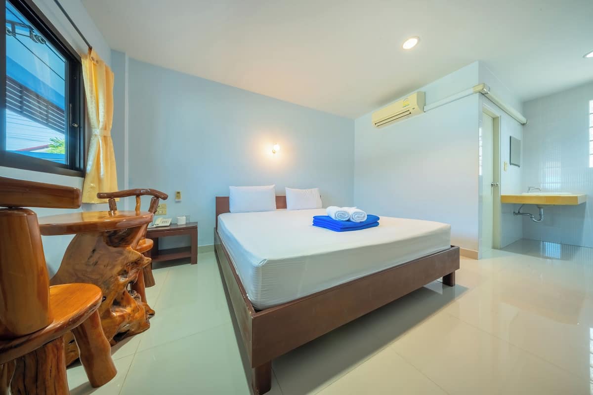 Ein Hotelzimmer mit einem hölzernen Bett, einem Schreibtisch mit Stuhl, einem Nachttisch und einem Badezimmer mit Waschbecken und Spiegel.