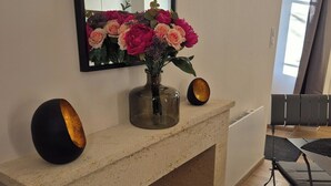 Una habitación con chimenea, un espejo, un jarrón con flores y un área de descanso con mesa y sillas.
