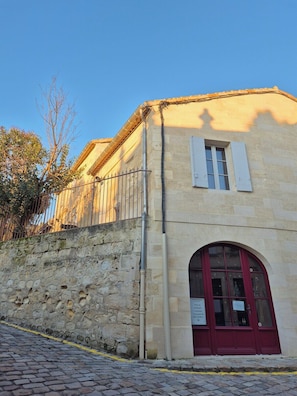 A stone building with a red door and a window with shutters. - Studio des " Caves de la Tour Du Roy" St Emilion (Saint-Émilion)