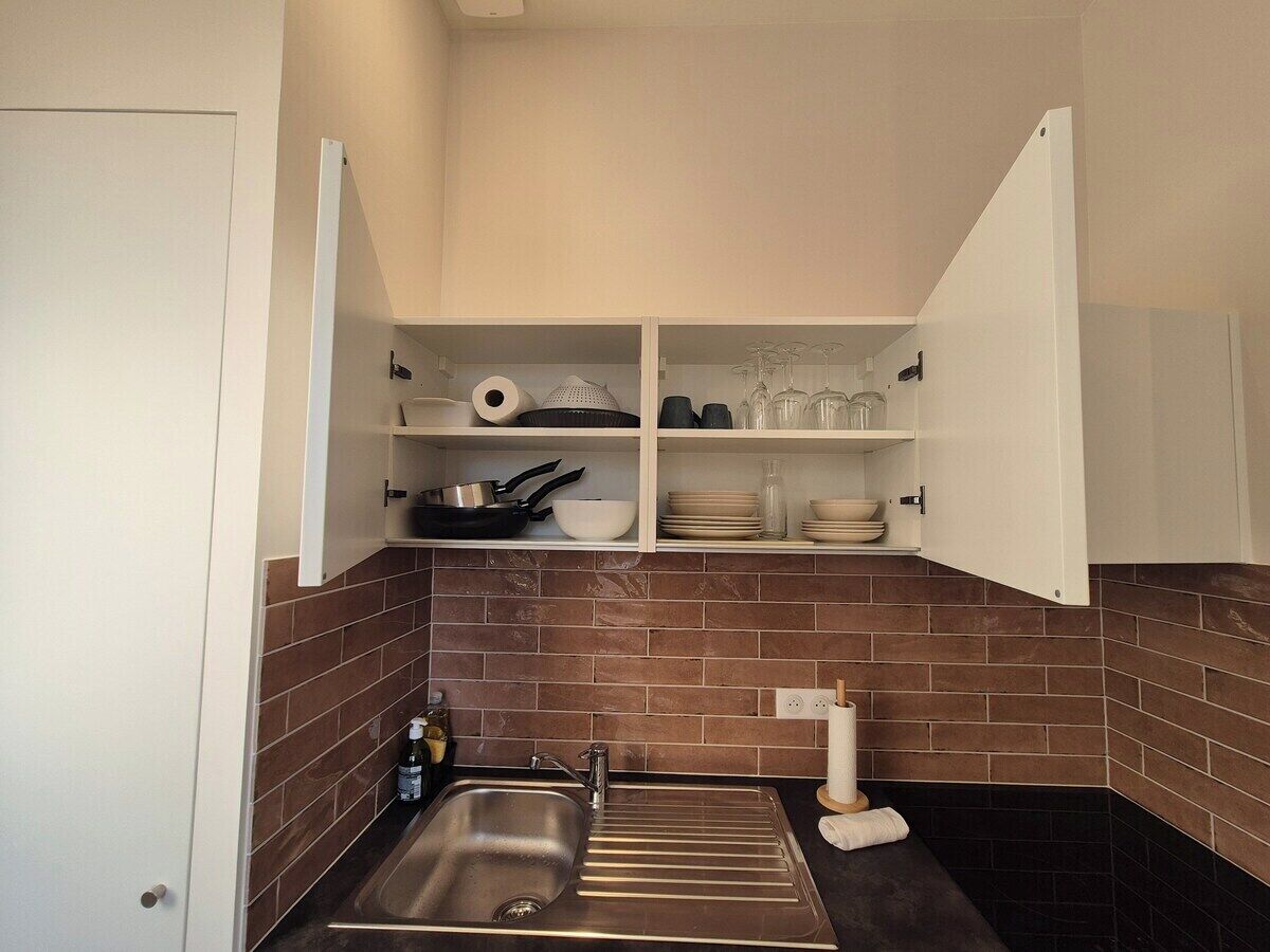 A compact kitchen with a sink, a stove, and open cabinets containing dishes and cookware.