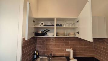 A compact kitchen with a sink, a stove, and open cabinets containing dishes and cookware.