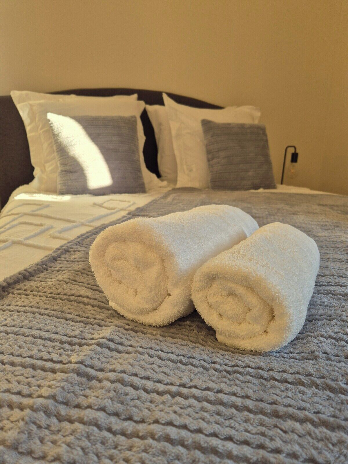 A bed with a textured blanket and two rolled towels.