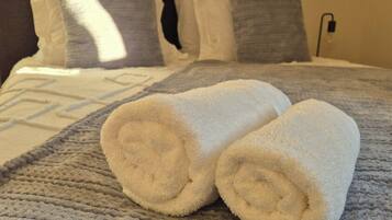 A bed with a textured blanket and two rolled towels.