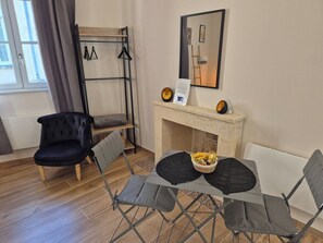 A room with a fireplace, a table with chairs, a black chair, and a coat rack. - Studio des " Caves de la Tour Du Roy" St Emilion (Saint-Émilion)