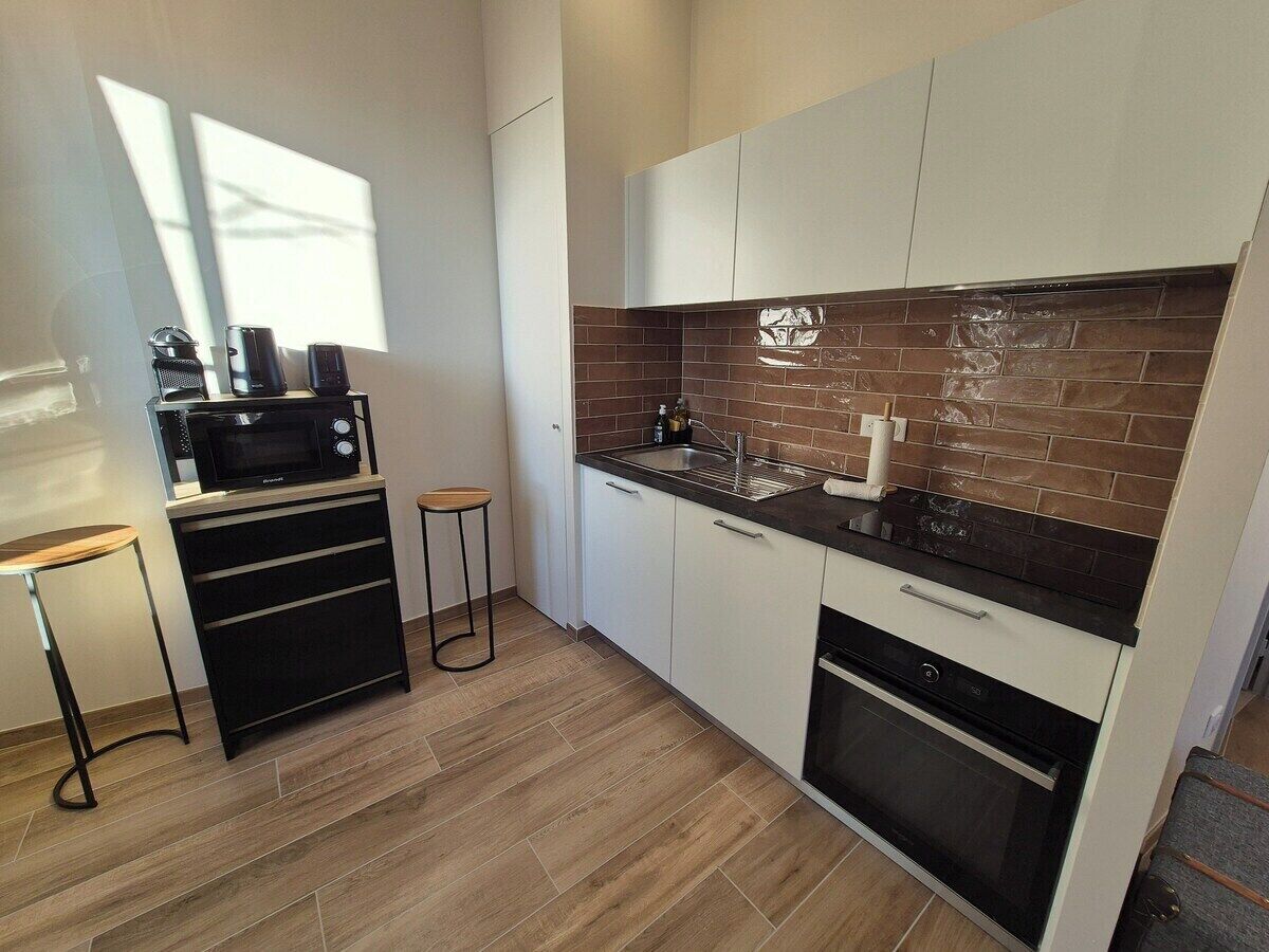 A modern kitchen with a microwave, stove, sink, and a small bar stool.