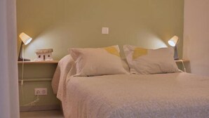 A bedroom with a bed, two bedside lamps, a nightstand with a lamp, and a wall socket. - SeafrontView · Cozy T1 Apartment - 3 (Praia)