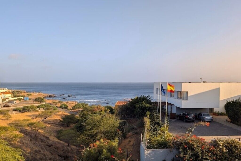 Una propiedad costera con un edificio moderno, una bandera y vista al mar.