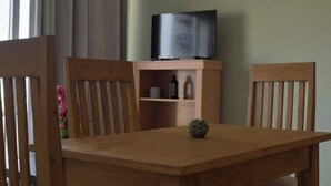 A wooden dining table with a television on a stand above it, two wooden chairs, and a small decorative item on the table. - SeafrontView · Cozy T1 Apartment - 3 (Praia)