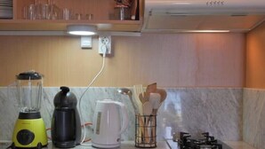 A kitchen with a blender, kettle, and utensils on the counter, a stove, and a wall-mounted outlet. - SeafrontView · Cozy T1 Apartment - 3 (Praia)