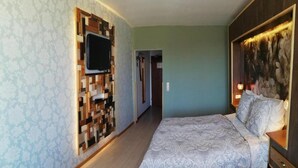 A bedroom with a bed, a TV mounted on a wooden panel wall, a door leading to another room, and a wall with a textured pattern. - Hotel Heiderhof by Belvilla- Double Room (Obersteinebach)