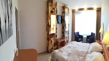 Quarto de hotel com cama, escrivaninha, cadeira, televisão e janela com cortinas.