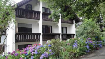 Ein zweistöckiges Gebäude mit Balkonen, umgeben von üppigem Grün und einer Vielzahl von Blumen.