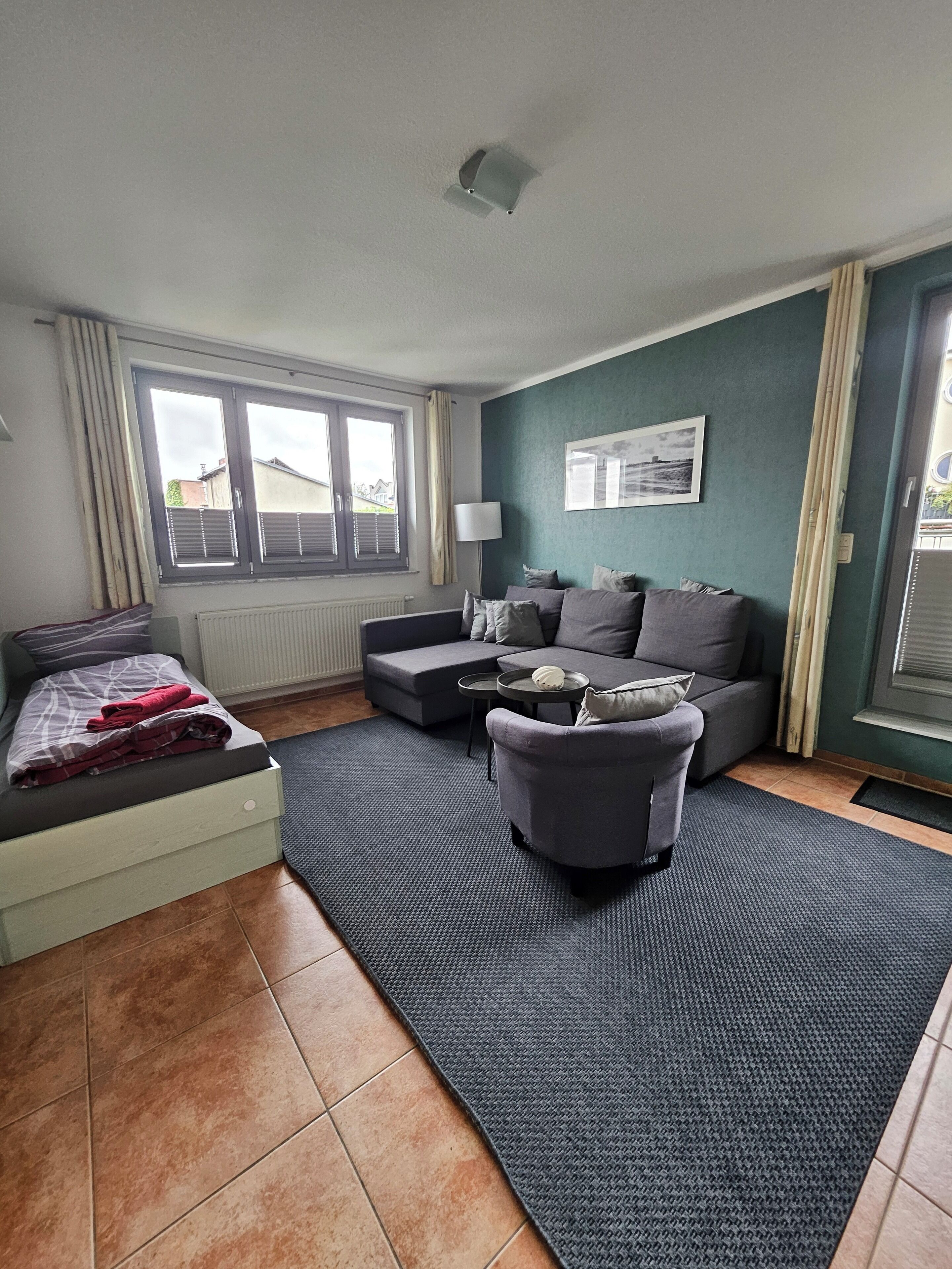 A modern living room with a sofa, a small table, a bed, and a window with curtains.