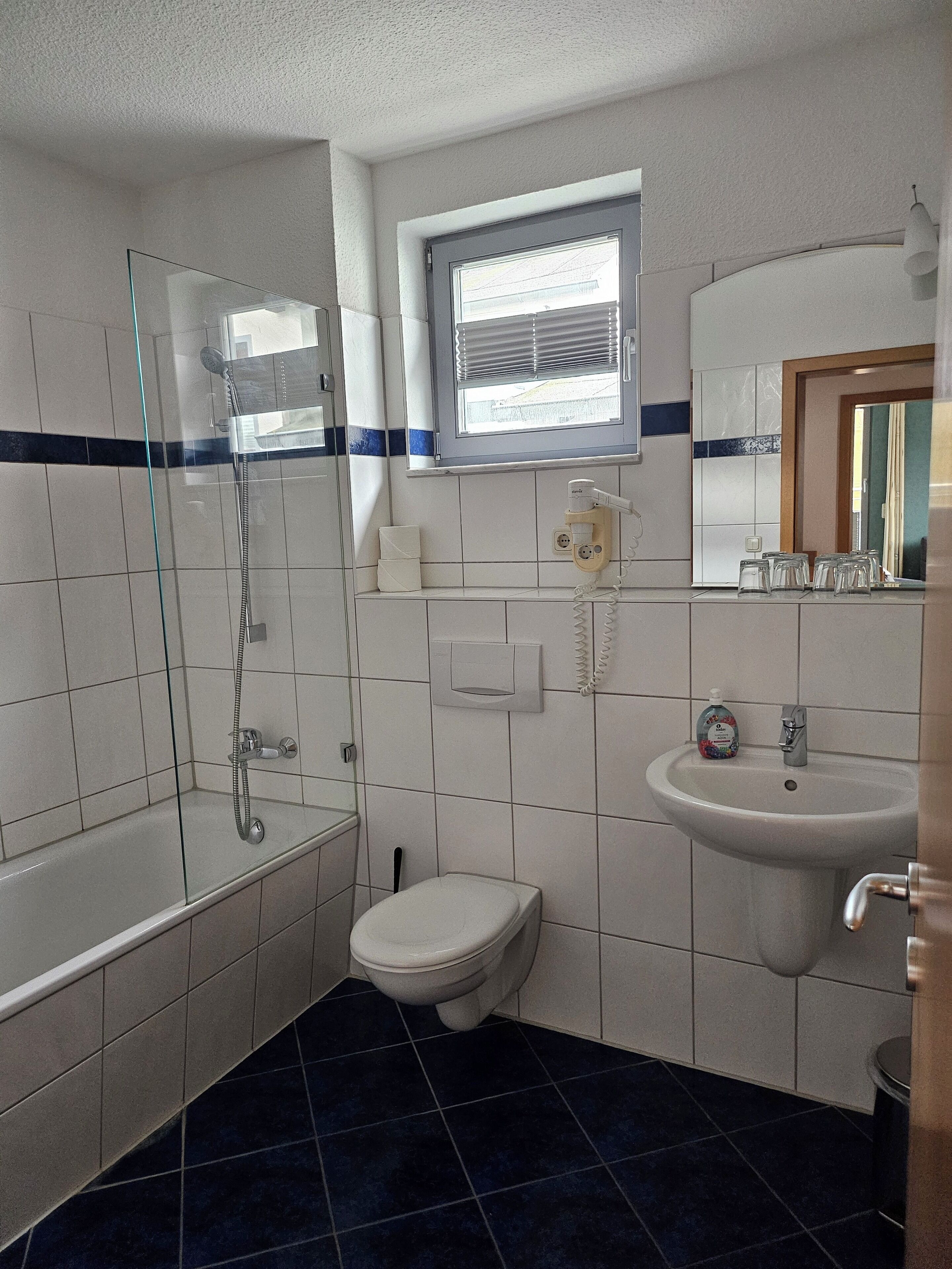 A bathroom with a glass-enclosed shower, a toilet, a sink, and a window above the sink.