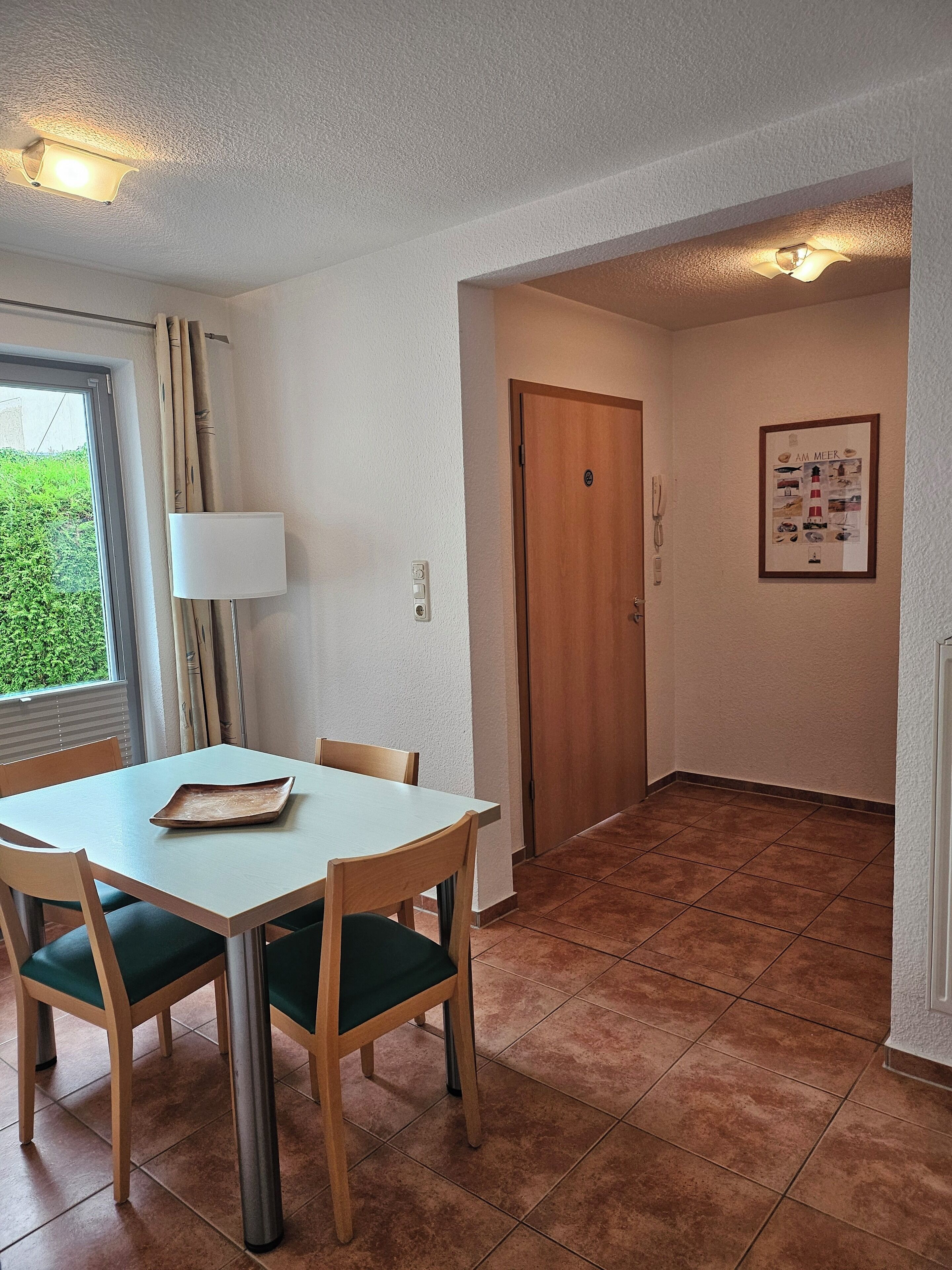 A dining area with a table and chairs, a window with curtains, a door, and a wall-mounted lamp.