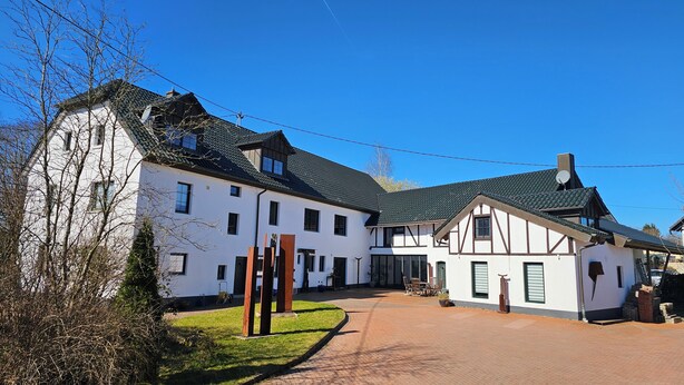 Ein weißes Gebäude mit dunklem Dach, einem gepflasterten Zugangsweg und blauem Himmel.