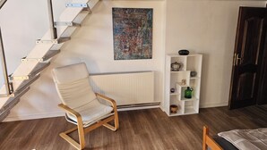 Ein Zimmer mit einem Holzhocker, einem Heizkörper, einem weißen Regal mit Dekorationen und einer Treppe.