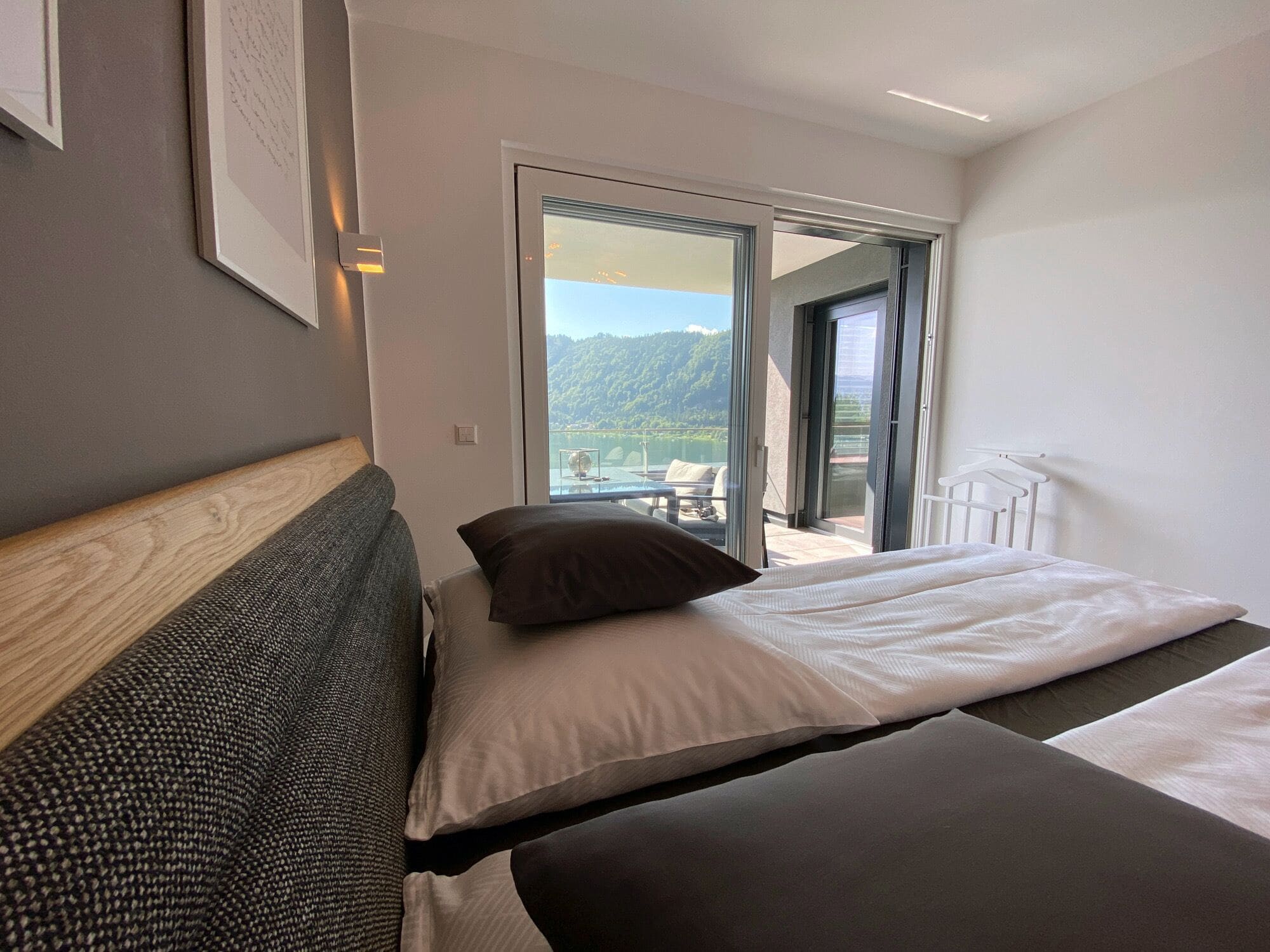 A modern hotel room with a large bed, a view of a balcony, and a mountain landscape.