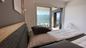 A modern hotel room with a large bed, a view of a balcony, and a mountain landscape.
