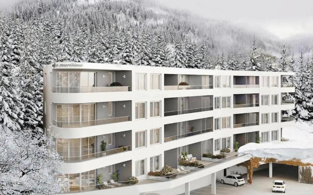A multi-story hotel with balconies, a covered parking area, and a snowy forest backdrop.