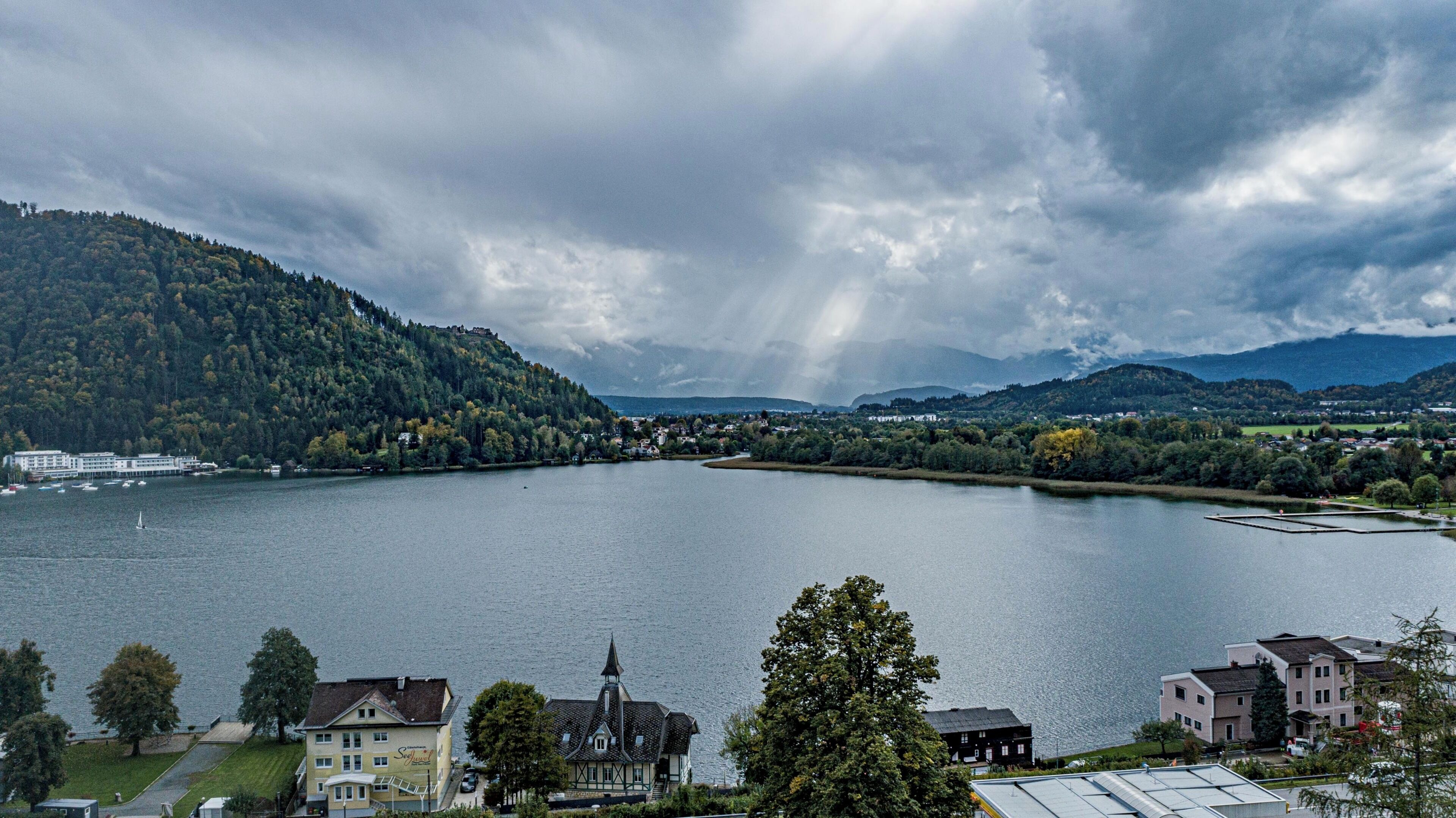 A lakeside view with a church, residential buildings, and a distant mountain range.
